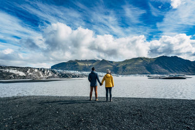 Rear view of two people on beach against sky