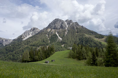 Scenic view of green landscape and mountains against cloudy sky on sunny day