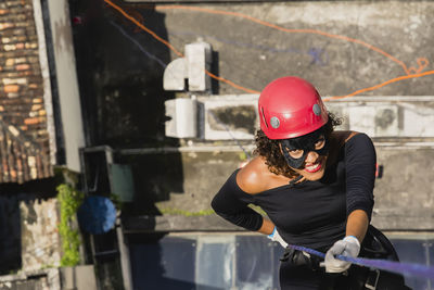 A woman wearing a hero costume with protective helmet walking down a tall rappel building. 