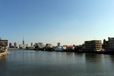 River by buildings in city against clear sky