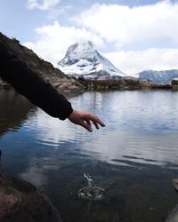 Person hand on snowcapped mountain by lake against sky