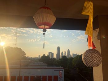 Illuminated lanterns hanging by buildings in city against sky during sunset
