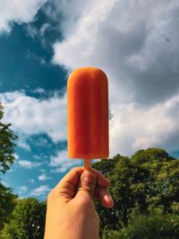 Close-up of hand holding ice cream against sky