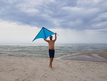 Full length of man flying kite while standing on beach against sky