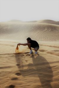 Full length of young man playing with sand at desert against clear sky