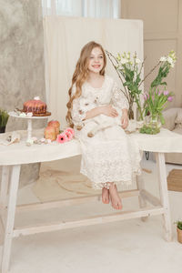 The girl is sitting at the easter table with cakes, spring flowers and quail eggs 