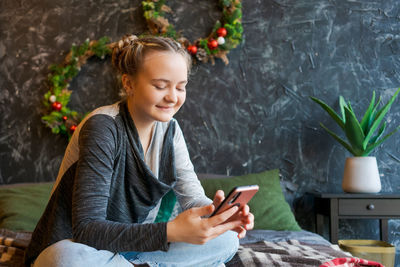 Thoughtful caucasian girl enjoying christmas eve at home using smart phone