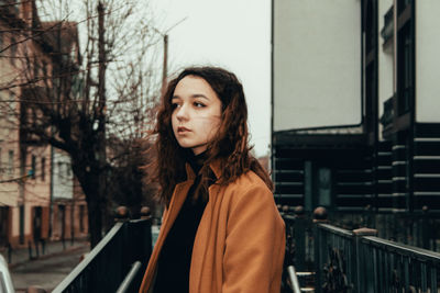 Portrait of young woman looking away while standing on railing