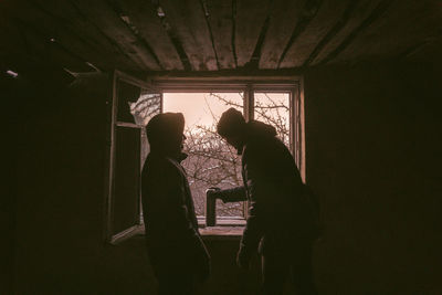 Rear view of silhouette man standing against window at home