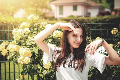 Portrait of smiling young woman standing against flowering plants during sunny day