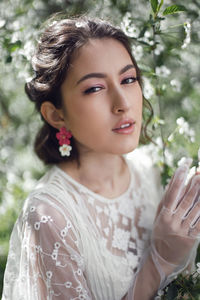 Portrait of a young beautiful woman in white clothes standing next to blooming cherry tree in spring