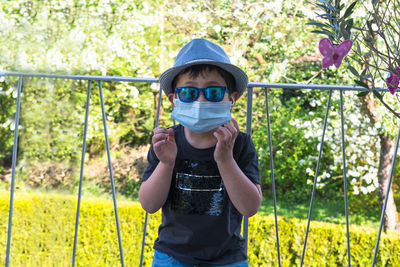 Portrait of boy wearing surgical mask while standing against railing