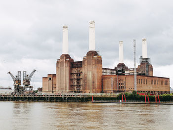 Factory by river against cloudy sky