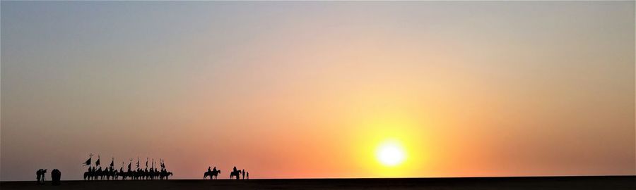 Panoramic view of silhouette people with domestic animals standing on field against sky during sunset