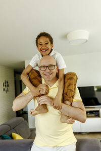 Smiling man carrying son on shoulder at home