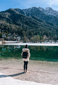 Rear view of female wearing winter clothes, standing on shore of lake jasna in slovenia