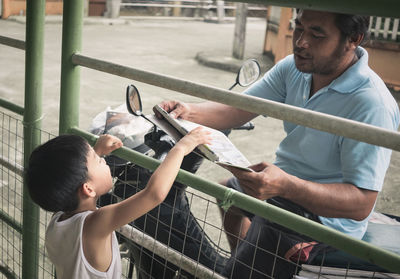 Boy receiving newspaper from delivery man while standing at gate