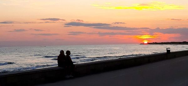 Silhouette people on beach against sky during sunset