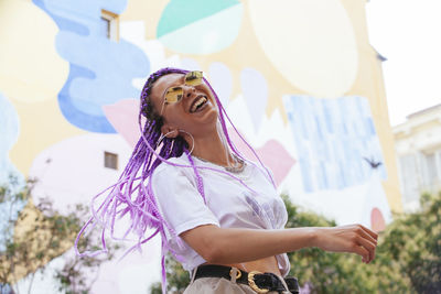 Low angle view of cheerful young woman standing in city