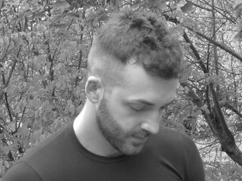 Portrait of young man looking away against trees