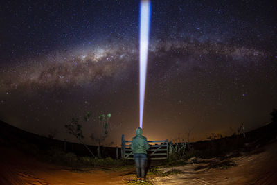 Rear view of woman with illuminated flashlight standing against star field at night