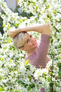 Young woman with pink hair poses by a blooming apple tree.