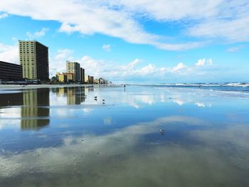 Reflection of buildings on beach against sky