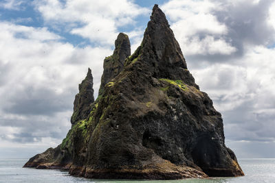 Low angle view of rock formation in sea against cloudy sky