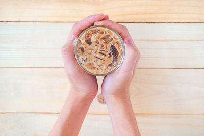 Top down of a man's hand holding a glass of iced coffee on the wooden table, iced coffee