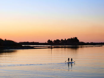 Silhouette people swimming in lake against sky during sunset