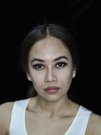 Close-up portrait of young woman against black background