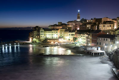 Illuminated buildings by sea against sky at night