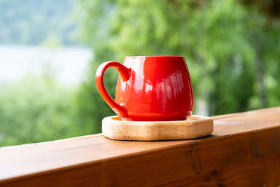 Morning coffee in garden. red mug on wooden board against blurred nature.