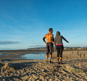 Rear view of friends standing on beach against sky