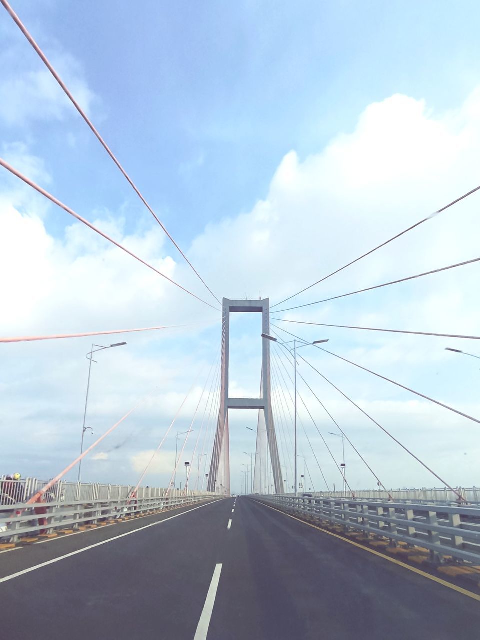 transportation, road, sky, bridge, architecture, cloud, built structure, city, suspension bridge, cable-stayed bridge, the way forward, nature, cable, travel, street, travel destinations, traffic, car, motor vehicle, highway, no people, line, mode of transportation, sign, vanishing point, cityscape, symbol, day, outdoors, city life, building exterior, diminishing perspective, road marking, tourism, blue, landscape, motion, marking, urban skyline, steel cable, land vehicle, cloudscape, water, sunlight