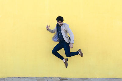Young man jumping in the air in front of yellow wall