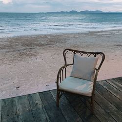 Empty chairs on beach by sea against sky