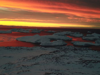 Scenic view of frozen lake against orange sky during sunset