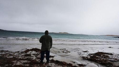 Rear view of man standing on beach against sky