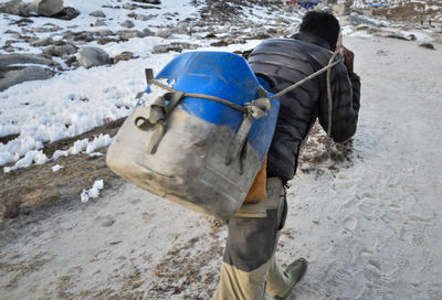 Rear view of man carrying plastic can while walking on snow covered field