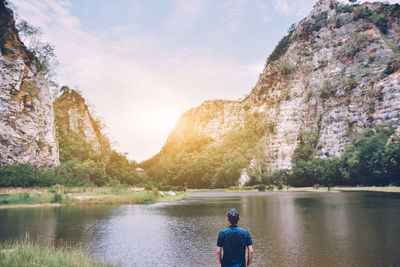 Rear view of man looking at mountains while standing by lake