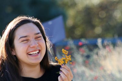 Close-up of cheerful young woman with flowers against blurred background