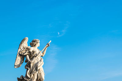 Low angle view of angel statue against blue sky