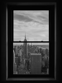 Buildings against cloudy sky seen through glass window