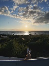 Rear view of woman sitting on beach against sky during sunset