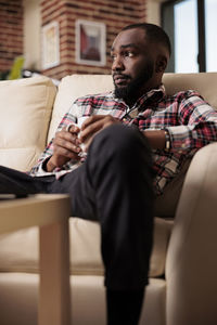 Portrait of young woman using mobile phone while sitting on sofa at home