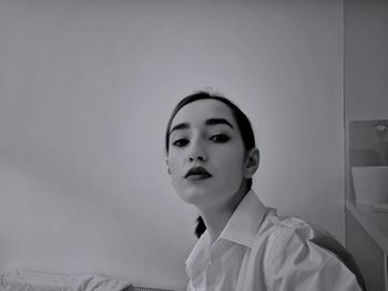 Portrait of young woman with make-up sitting against wall at home