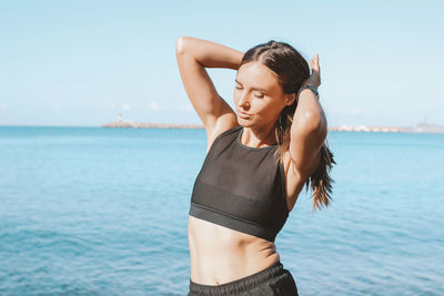 Young woman standing at beach against sky