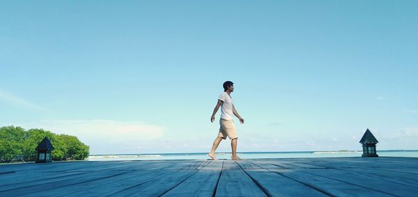 Rear view of woman standing on pier against blue sky