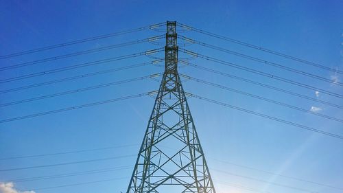 Low angle view of electricity pylon against clear blue sky